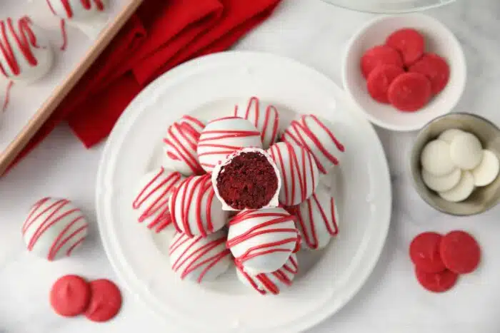 Red Velvet Truffles on a plate with one cut open showing the red cake inside of the white chocolate shell.