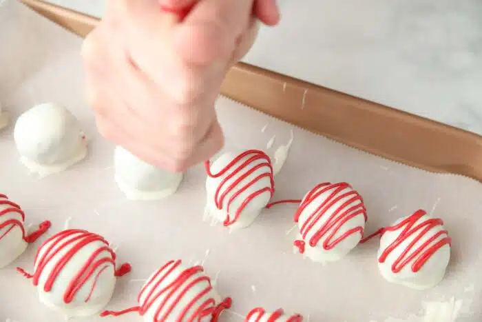 Piping red candy melts over the white chocolate covered red velvet truffles.