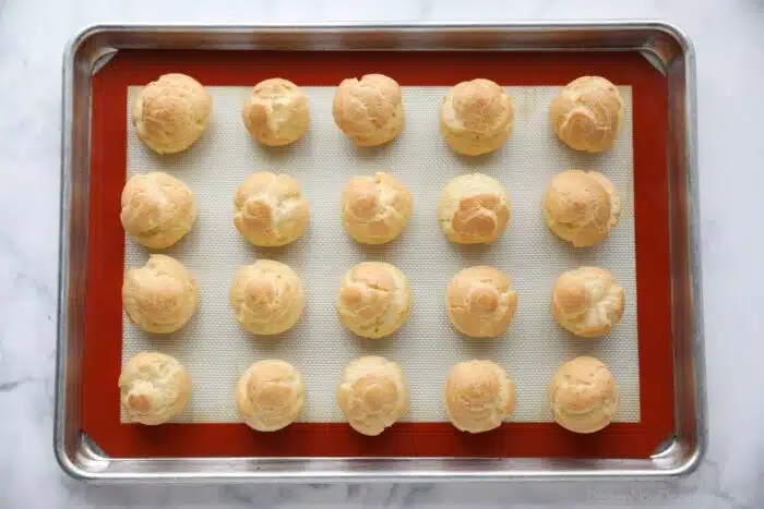 Baked cream puffs on a sheet tray.