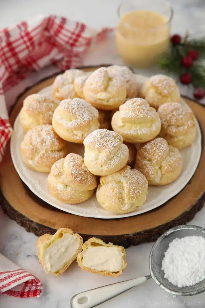 Eggnog cream puffs on a plate with one cut open showing the filling inside.