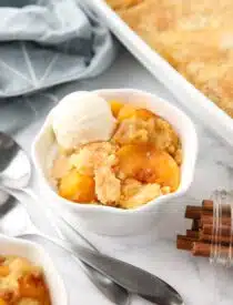 Peach dump cake (aka peach cobbler with cake mix) in a bowl with a scoop of vanilla ice cream.