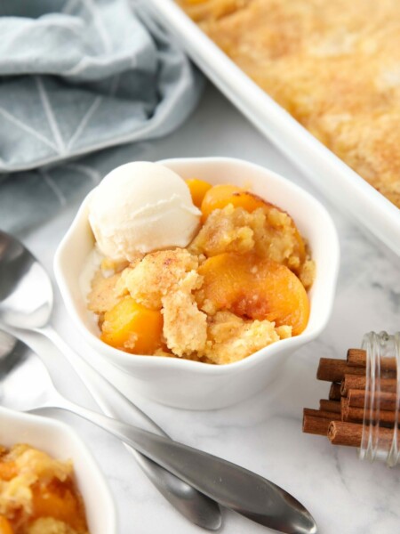 Peach dump cake (aka peach cobbler with cake mix) in a bowl with a scoop of vanilla ice cream.