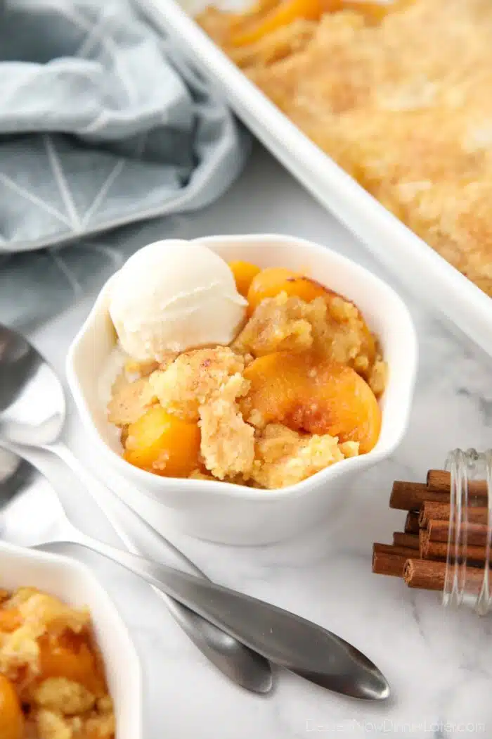 Peach dump cake (aka peach cobbler with cake mix) in a bowl with a scoop of vanilla ice cream.