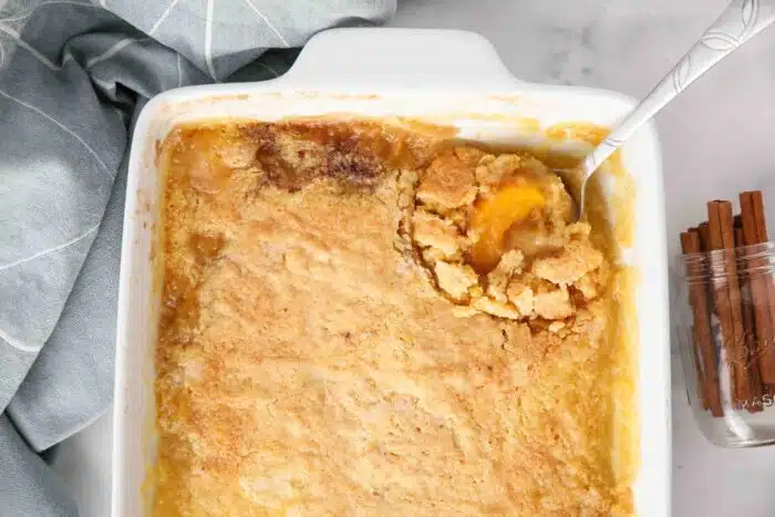 Top view of peach dump cake in pan being scooped with a spoon.