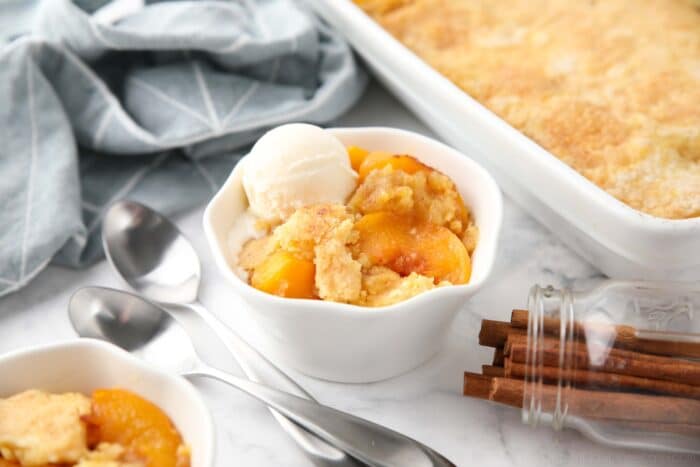 Peach dump cake (aka peach cobbler with cake mix) in a bowl with a scoop of vanilla ice cream.