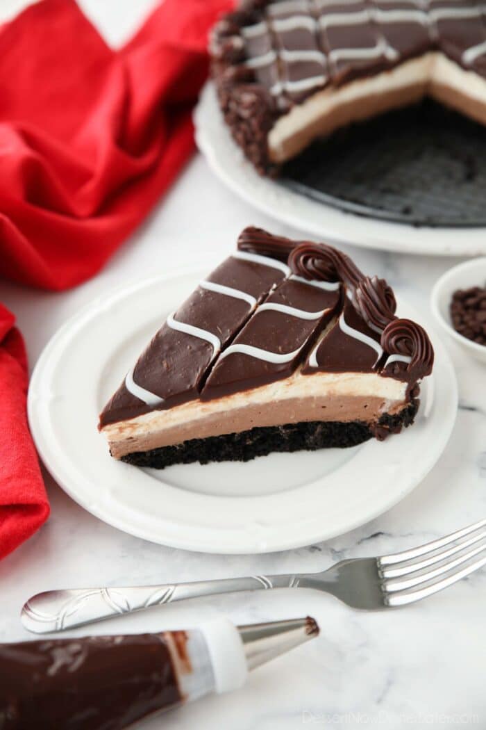 Slice of Olive Garden Black Tie Mousse Cake on a plate showing layers of chocolate cake, chocolate mousse, vanilla mousse, with swirled white and dark chocolate ganache on top.