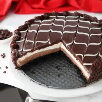 Copycat Olive Garden Black Tie Mousse Cake missing a couple of pieces to show layers of chocolate cake, chocolate mousse, vanilla mousse, with swirled white and dark chocolate ganache on top.