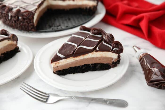 Slice of Olive Garden Black Tie Mousse Cake on a plate showing layers of chocolate cake, chocolate mousse, vanilla mousse, with swirled white and dark chocolate ganache on top.