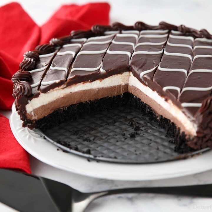 Copycat Black Tie Mousse Cake missing a couple of pieces to show layers of chocolate cake, chocolate mousse, vanilla mousse, with swirled white and dark chocolate ganache on top.