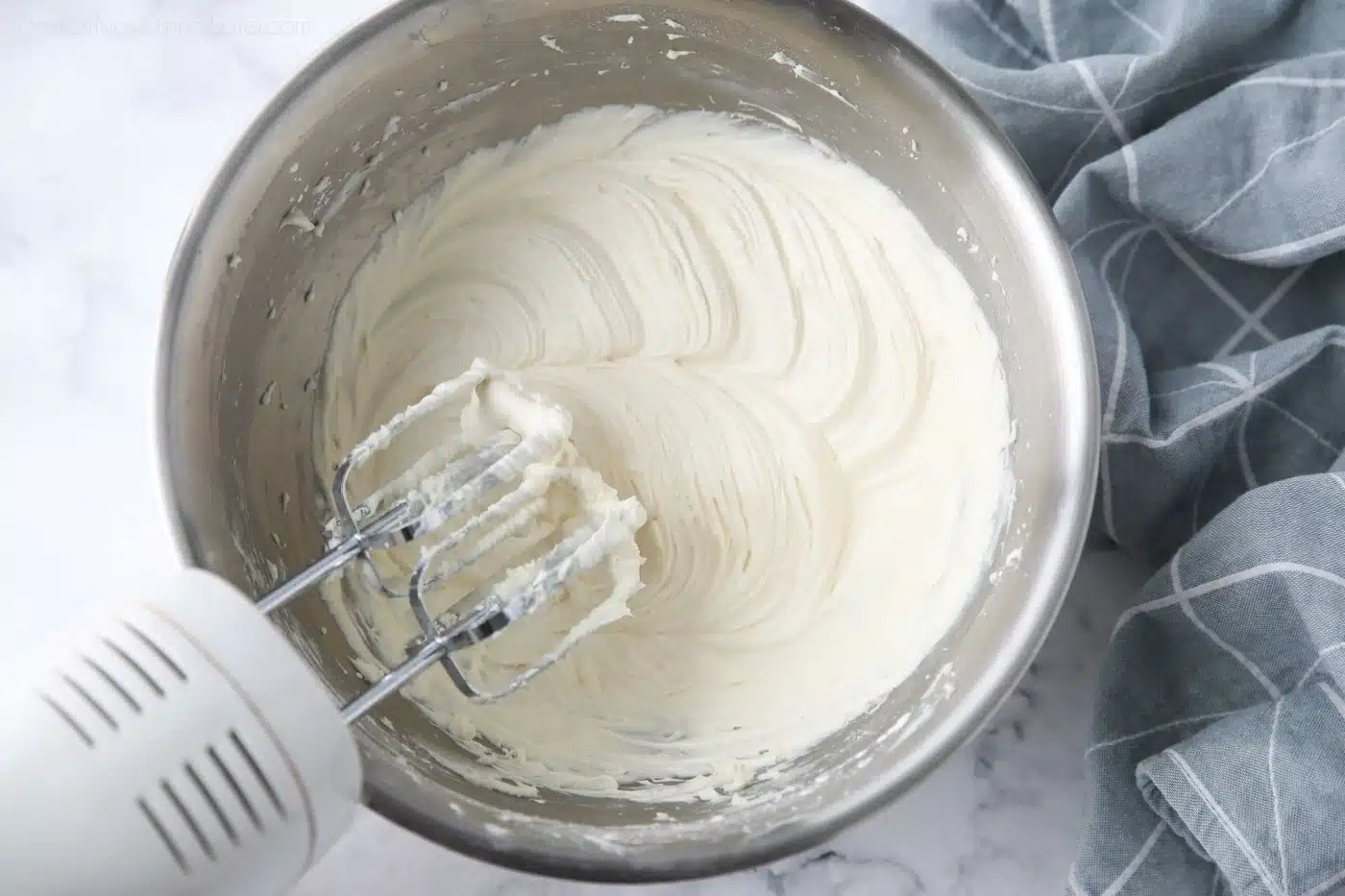 Cream cheese frosting made in a bowl with an electric hand mixer.