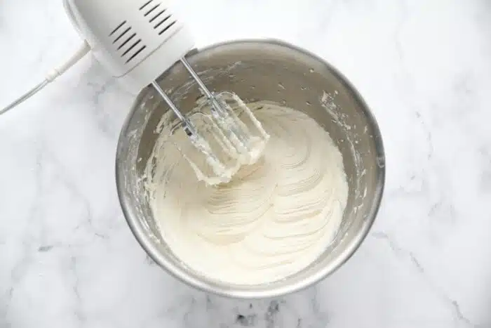 The best cream cheese frosting recipe made in a bowl with an electric hand mixer.