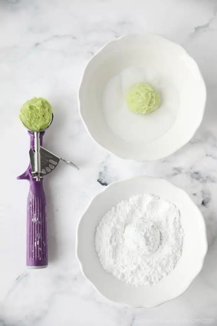 Scoop of lime cookie dough being coated with granulated sugar, and then powdered sugar.