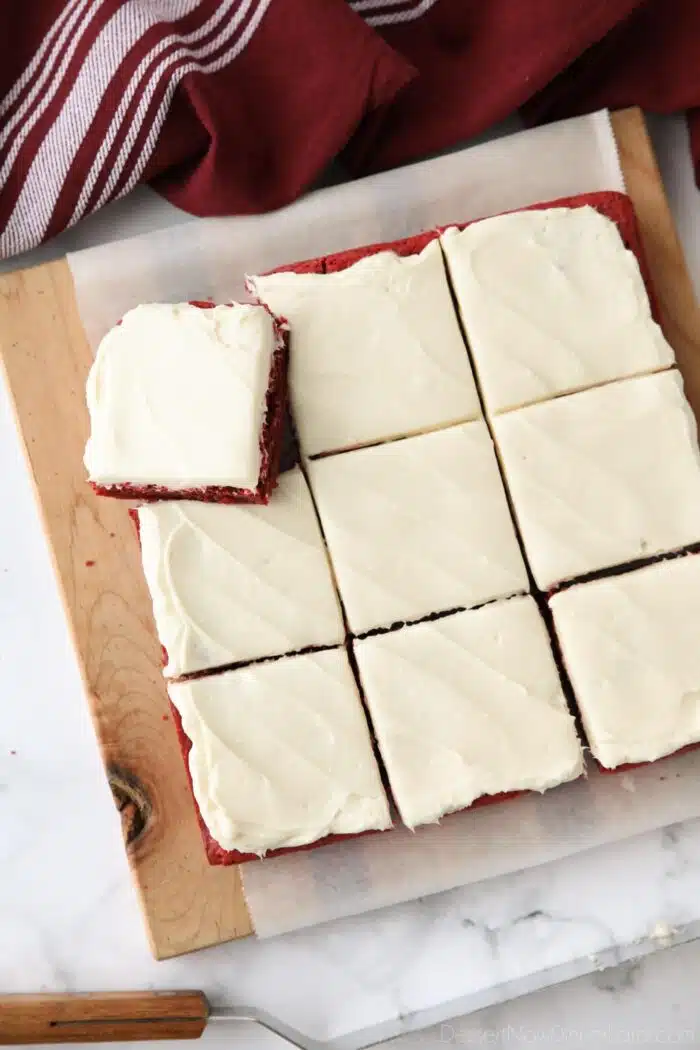 Square pan of Red Velvet Brownies with cream cheese frosting cut into squares on a cutting board.