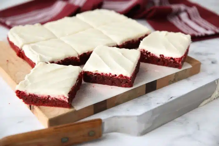 Square pan of Red Velvet Brownies with cream cheese frosting cut into squares on a cutting board.