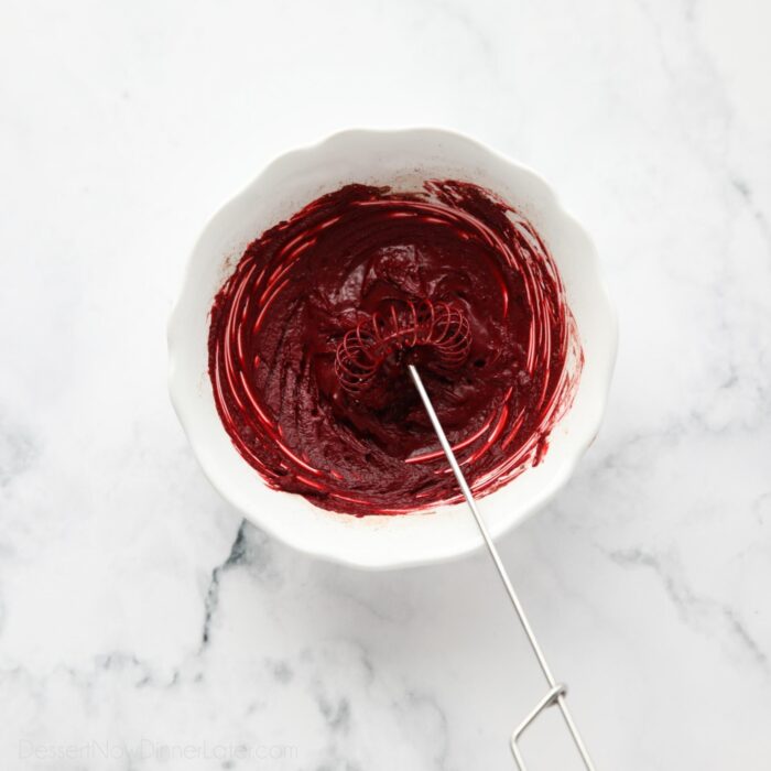 Red cocoa paste in a bowl with a whisk.