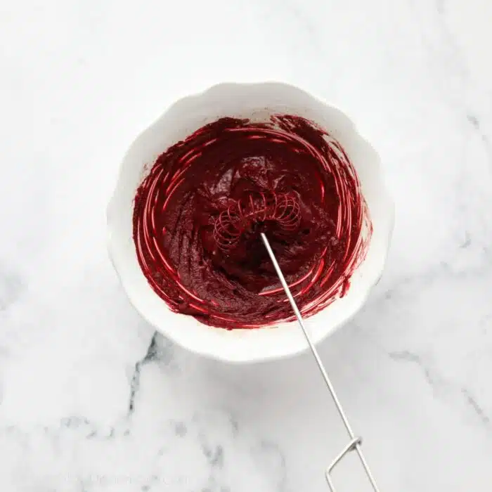 Red cocoa paste in a bowl with a whisk.