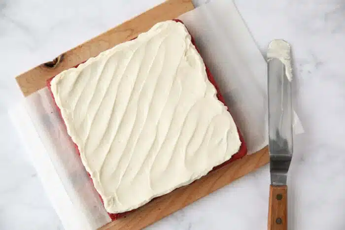 Cream cheese frosting spread on top of red velvet brownies.