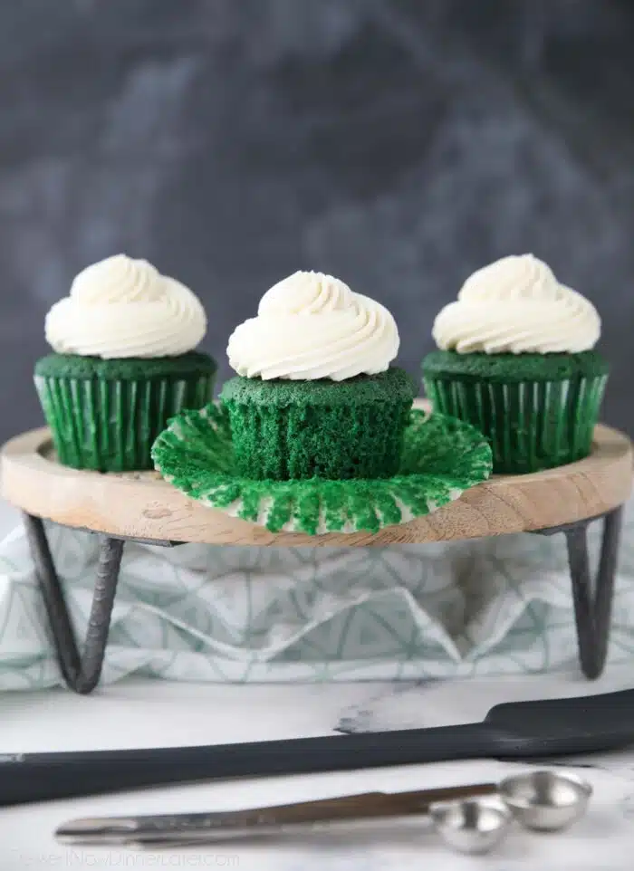 Green velvet cupcakes on a cake stand. One with the wrapper pulled down.