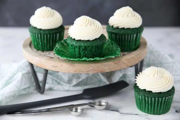Green velvet cupcakes on a cake stand. One with the wrapper pulled down.