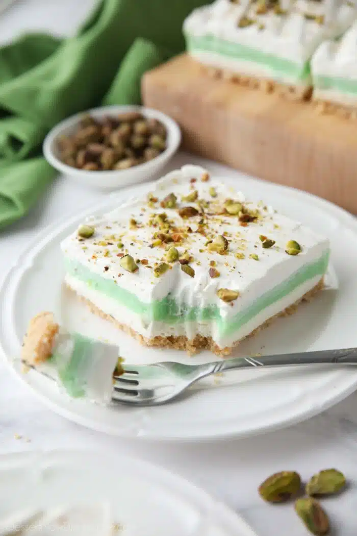 Layered pistachio dessert on a plate with a fork-full taken out.