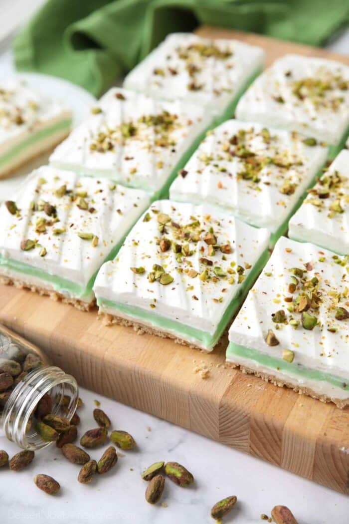 Side view of squares of layered pistachio dessert on a cutting board.