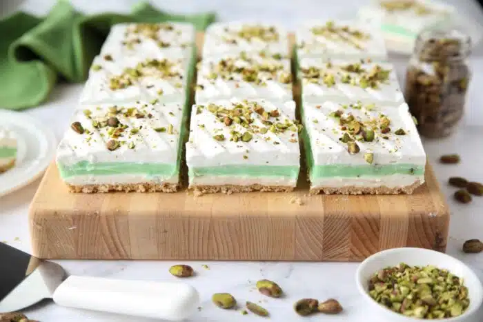 Side view of squares of layered pistachio dessert on a cutting board.