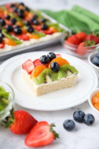 Square of sugar cookie fruit pizza on a plate.