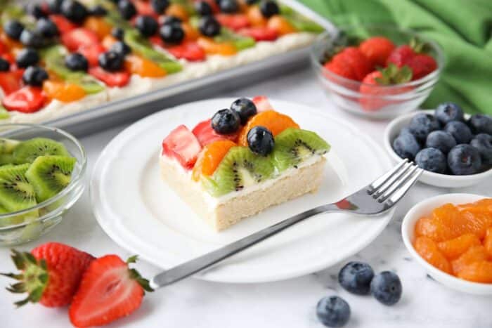 Square of sugar cookie fruit pizza on a plate with a fork.