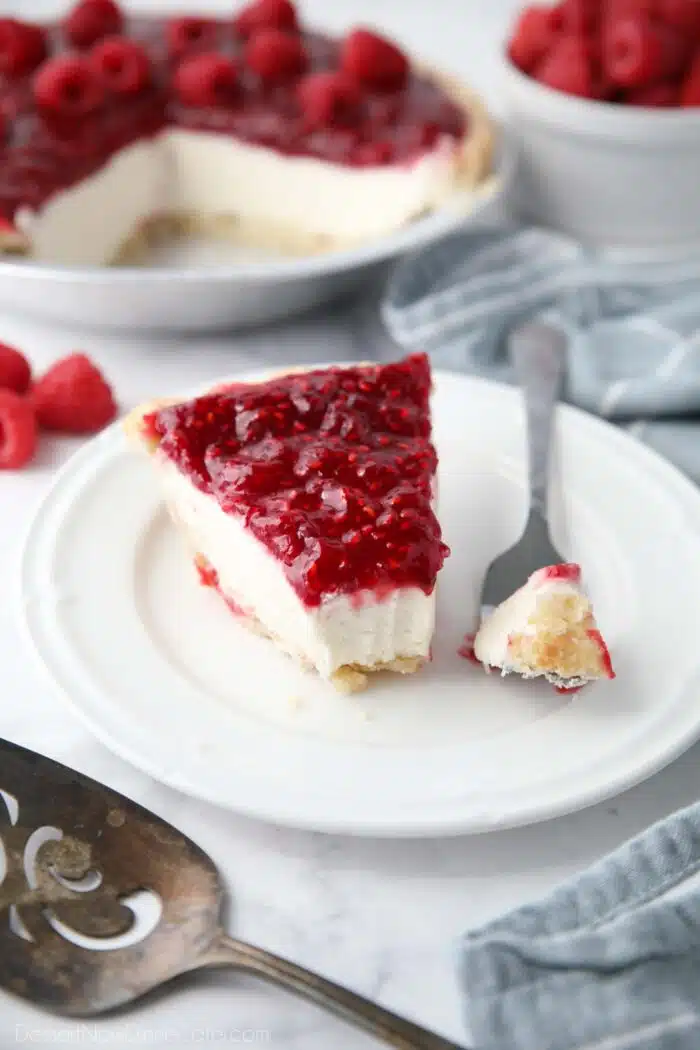 Slice of Raspberry Cream Pie on a plate with a forkful taken out to show layers of pastry crust, whipped cream cheese filling, and raspberry topping.