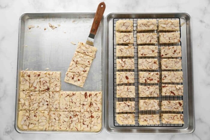 Transferring almond bars to a wire rack inside of a sheet pan.