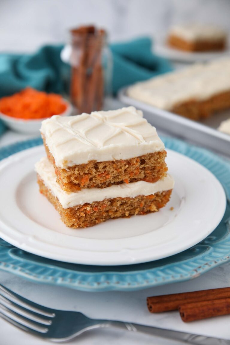 Two carrot cake bars with frosting stacked on a plate.