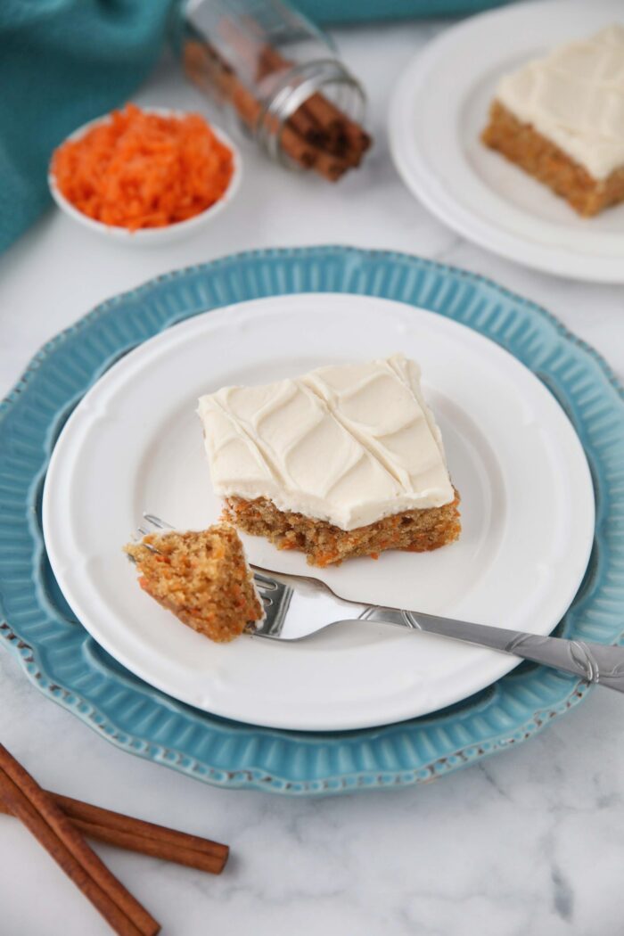A single carrot cake bar with maple frosting on a plate with a forkful taken out.