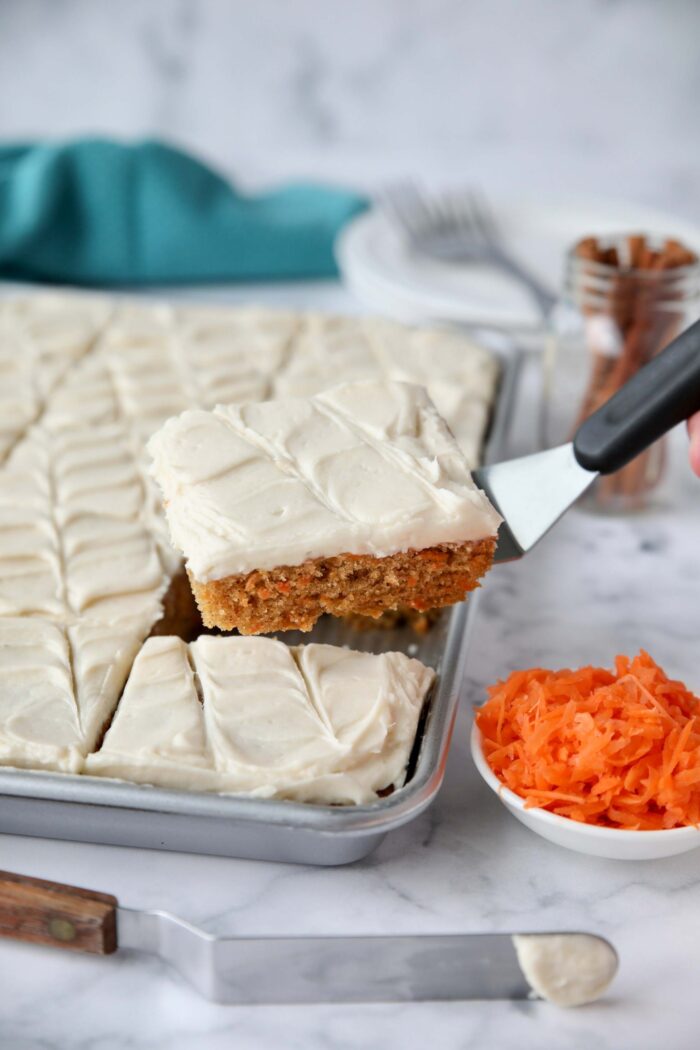 Carrot cake bars being scooped out of a sheet pan with a serving spatula.