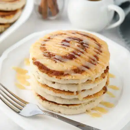 Stack of cinnamon roll pancakes with cream cheese glaze drizzled on top.