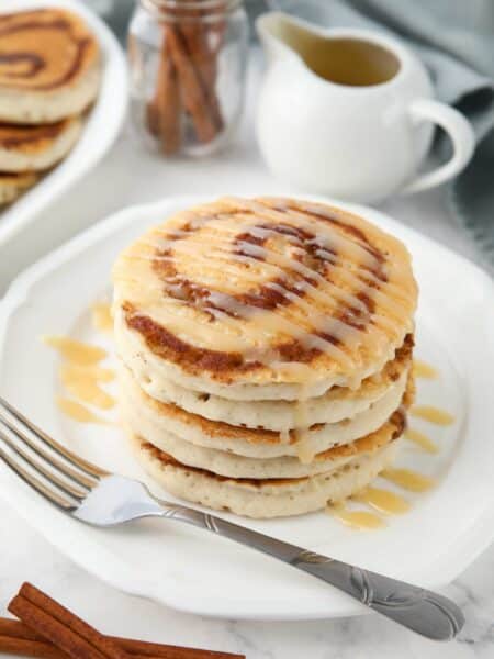 Stack of cinnamon roll pancakes with cream cheese glaze drizzled on top.