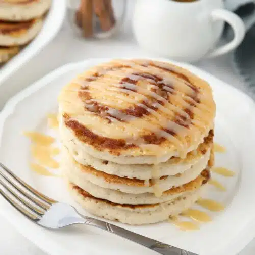 Stack of cinnamon roll pancakes with cream cheese glaze drizzled on top.