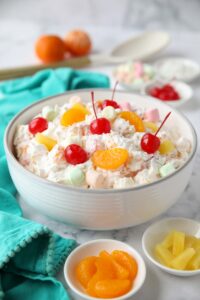 Bowl full of ambrosia salad with canned mandarin oranges, pineapple tidbits, maraschino cherries, shredded coconut, mini marshmallows, Greek yogurt and Cool Whip.