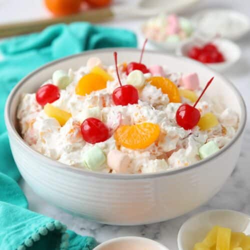 Bowl full of ambrosia salad with canned mandarin oranges, pineapple tidbits, maraschino cherries, shredded coconut, mini marshmallows, Greek yogurt and Cool Whip.