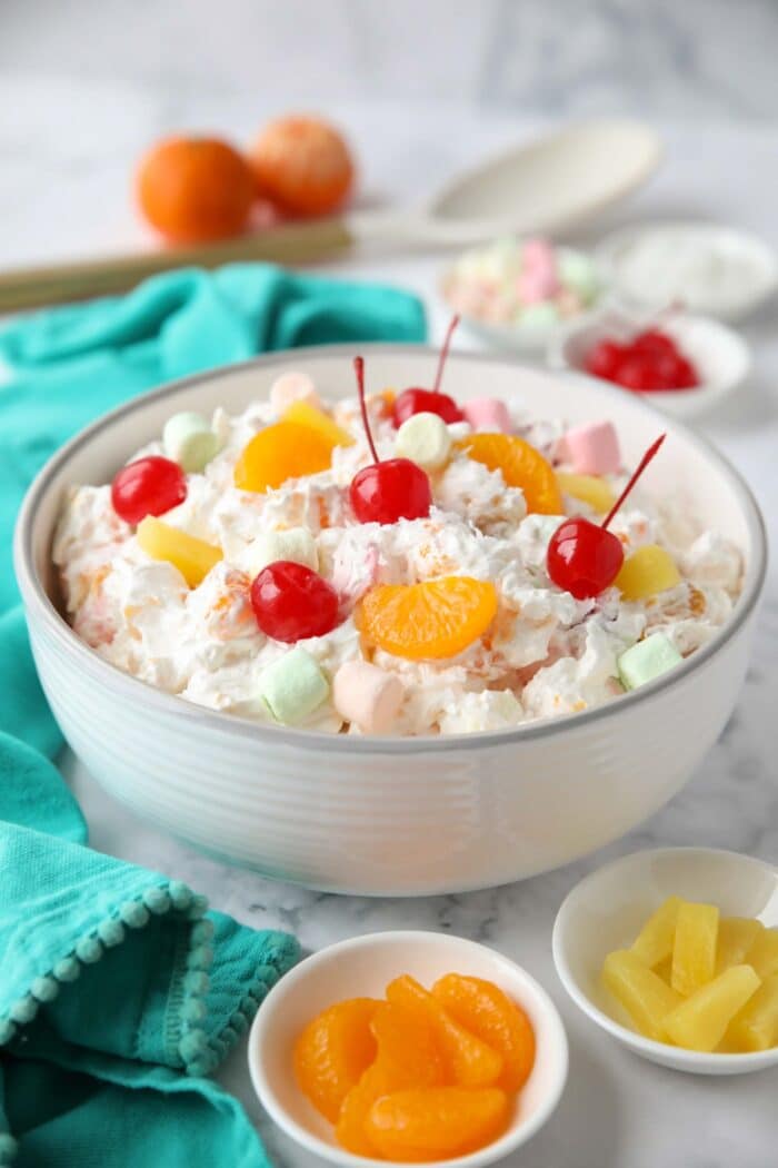 Bowl full of ambrosia salad with canned mandarin oranges, pineapple tidbits, maraschino cherries, shredded coconut, mini marshmallows, Greek yogurt and Cool Whip.