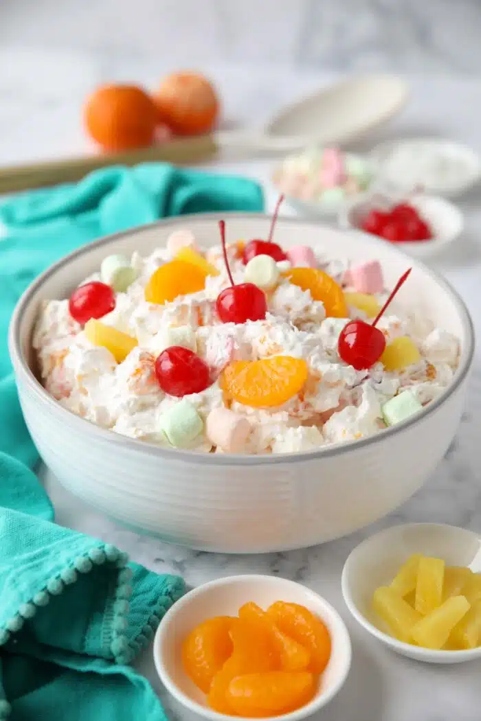 Bowl full of ambrosia salad with canned mandarin oranges, pineapple tidbits, maraschino cherries, shredded coconut, mini marshmallows, Greek yogurt and Cool Whip.
