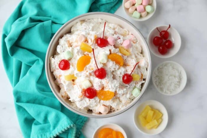 Top view of ambrosia fruit salad in a bowl with canned mandarin oranges, pineapple tidbits, maraschino cherries, shredded coconut, mini marshmallows, Greek yogurt and Cool Whip.
