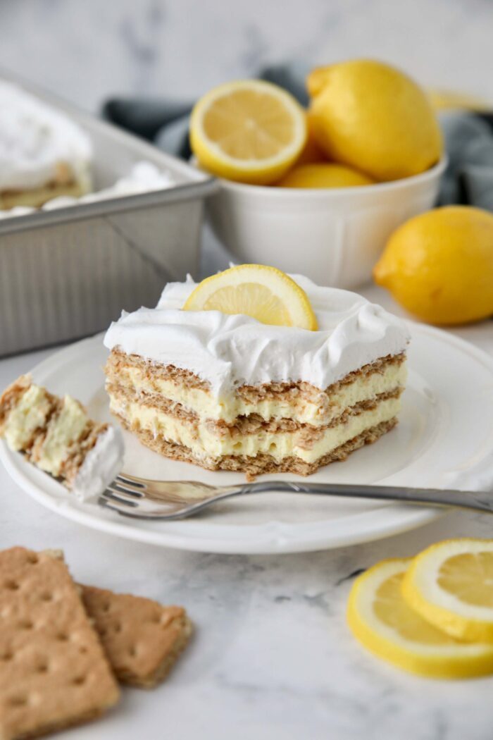 Forkful removed from a slice of lemon icebox cake layered with graham crackers, pudding, and whipped topping.