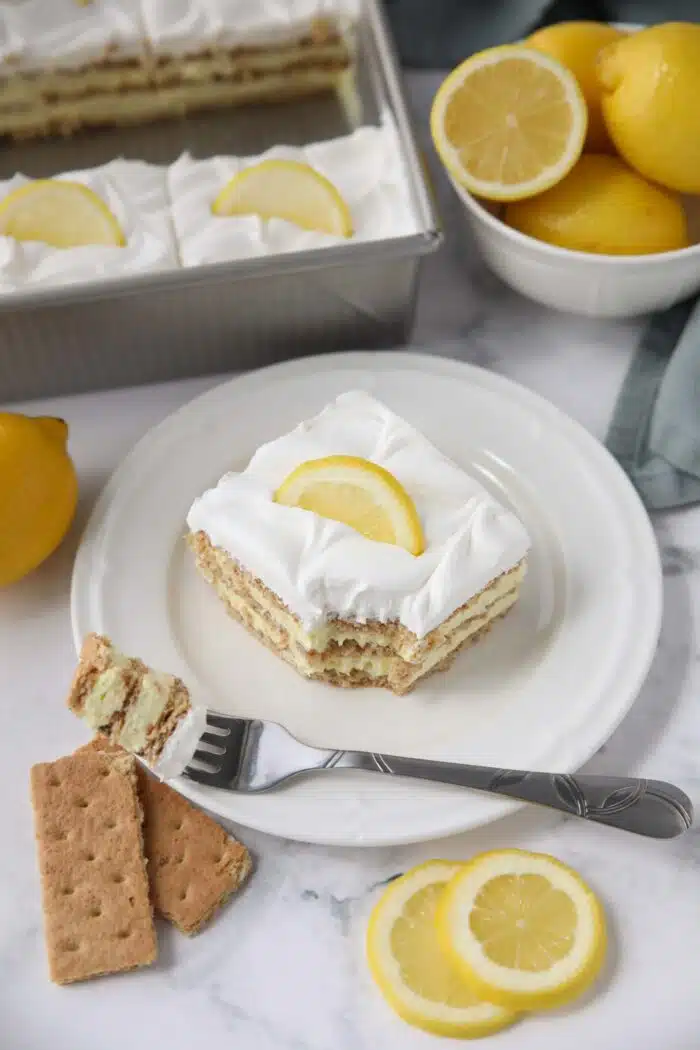 Forkful removed from a slice of lemon icebox cake layered with graham crackers, lemon pudding, and Cool Whip.