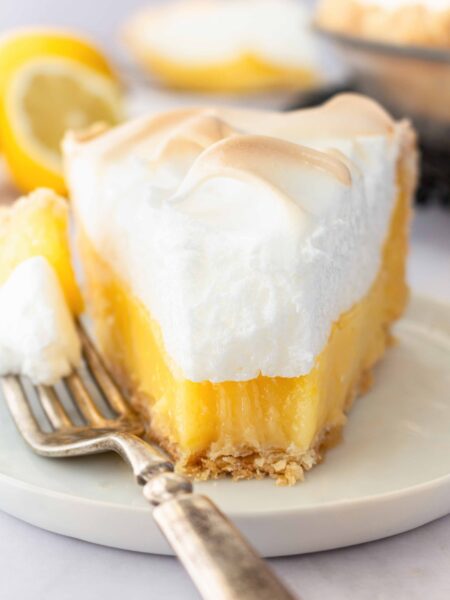 Slice of lemon meringue pie on a plate with a forkful taken out.