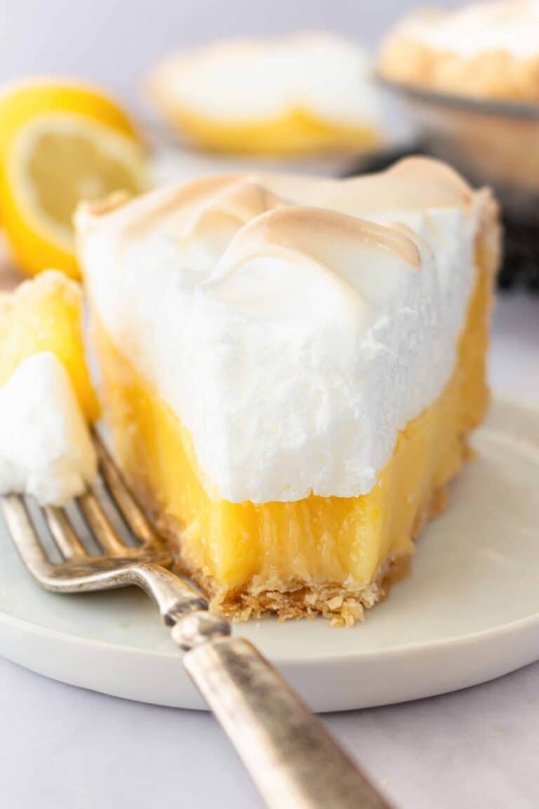 Slice of lemon meringue pie on a plate with a forkful taken out.