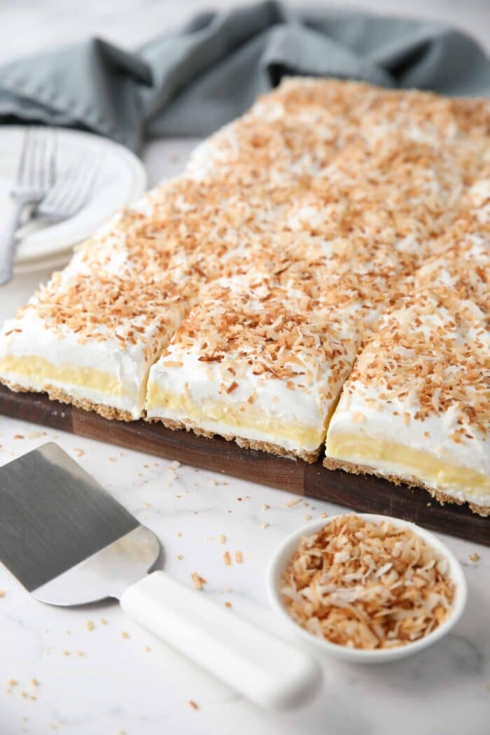 Coconut lush dessert with layers of graham cracker crust, cream cheese, coconut pudding, whipped topping, and toasted coconut.