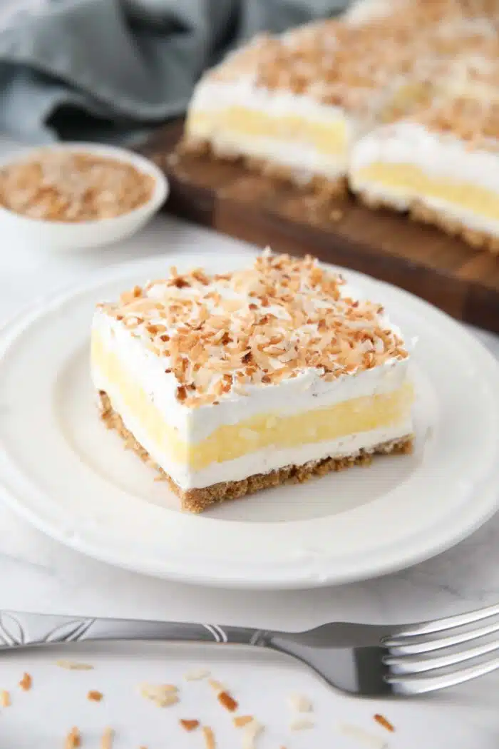 Coconut cream bars with layers of graham cracker crust, cream cheese, coconut pudding, whipped topping, and toasted coconut.