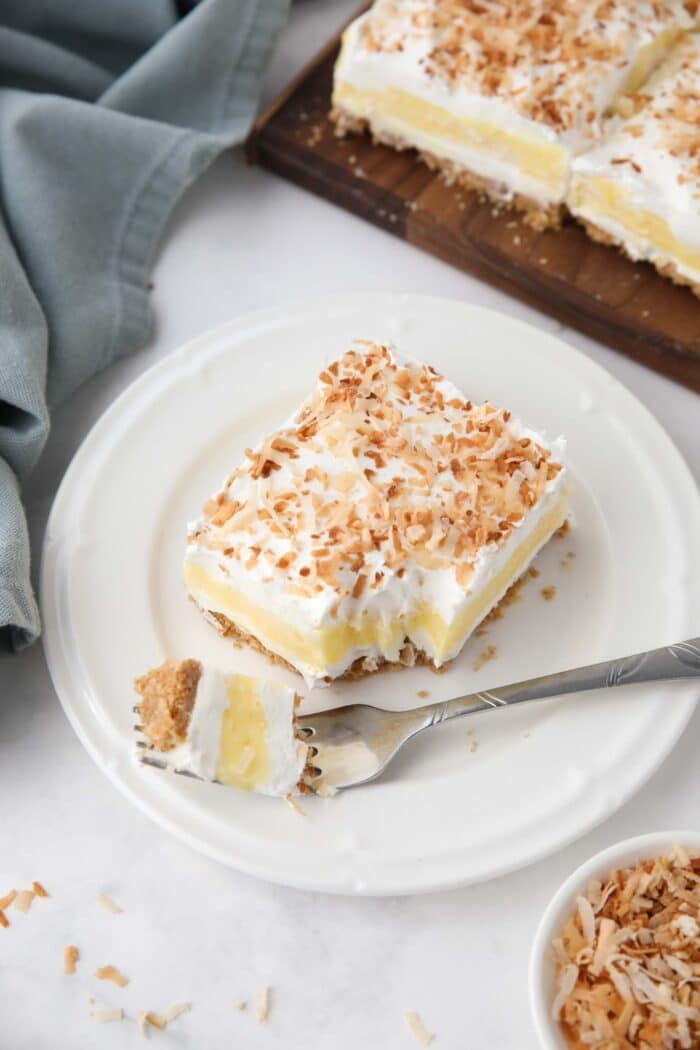 Slice of coconut cream bars on a plate with a forkful taken out.