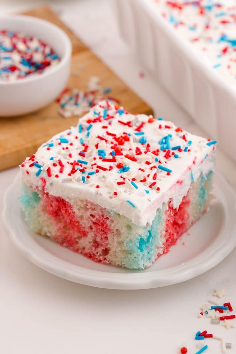 Red white and blue poke cake on a plate with Cool Whip and patriotic sprinkles on top.