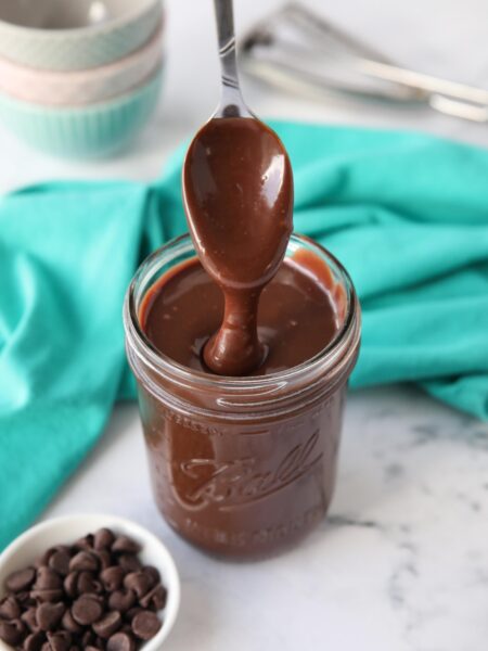 Homemade hot fudge recipe in a mason jar being drizzled with a spoon.
